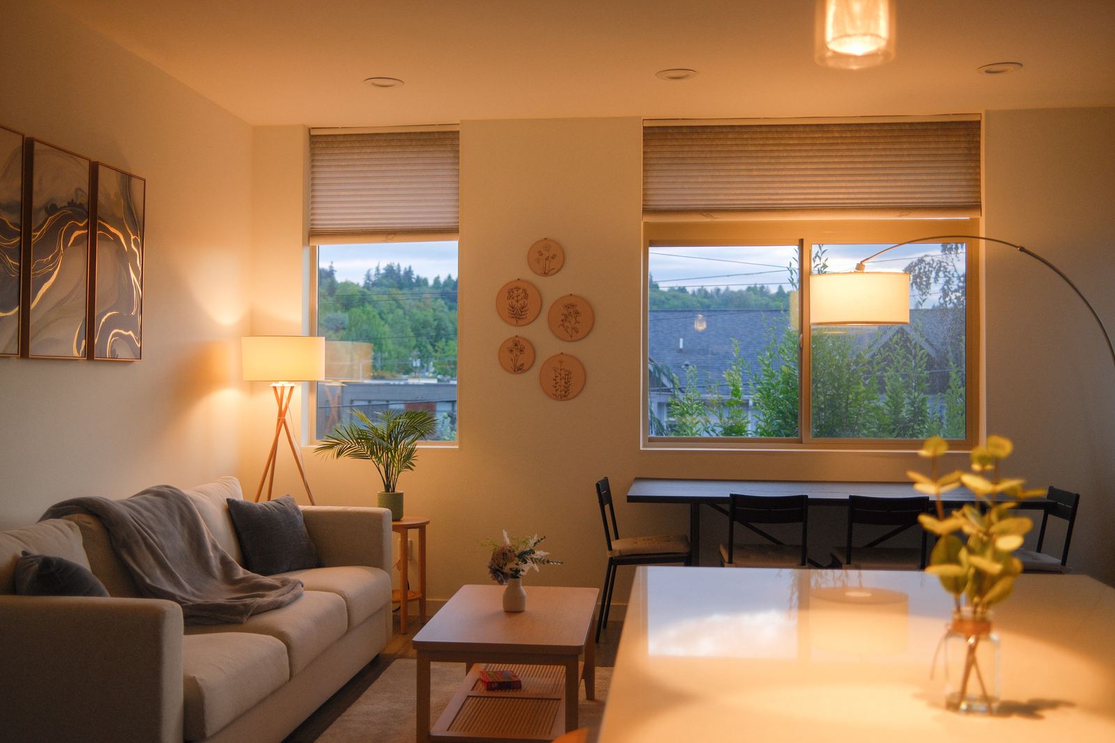 Light-filled living room with sofa, dining table, and treetop views